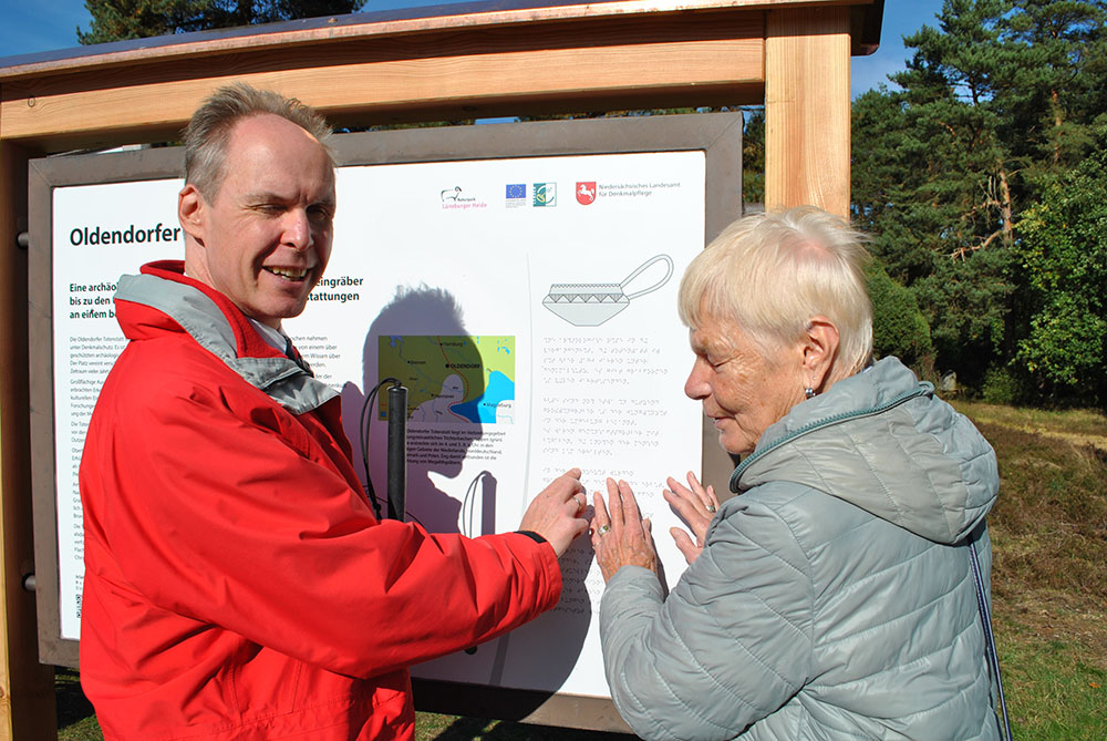 Sascha Paul und Helga Neumann, Mitglieder des Blinden- und Sehbehindertenverband Niedersachsen, lesen das neuen Informationsschild in der Oldendorfer Totenstatt. 